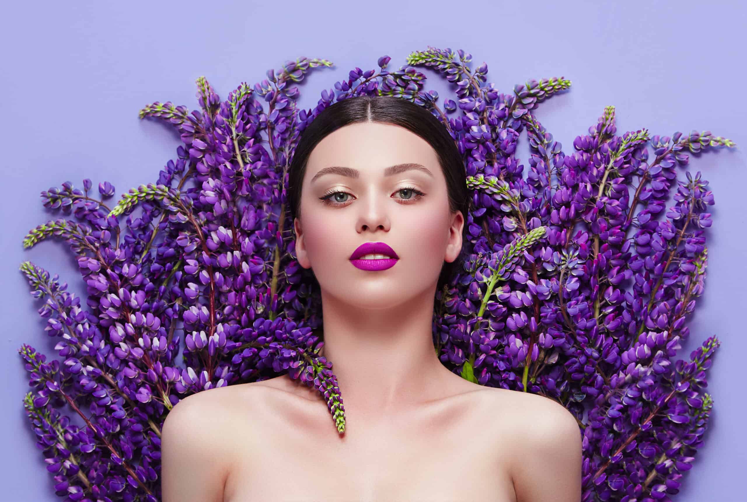 Beautiful young girl is surrounded by purple flowers. Blue flowers. Lilac lipstick. Cosmetic products for skin care. Health, beauty, cosmetics. A bouquet of flowers, beautiful hair.ir.